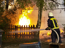 Ein Feuerwehmann bei Lscharbeiten vor einem Flammen-Hintergrund